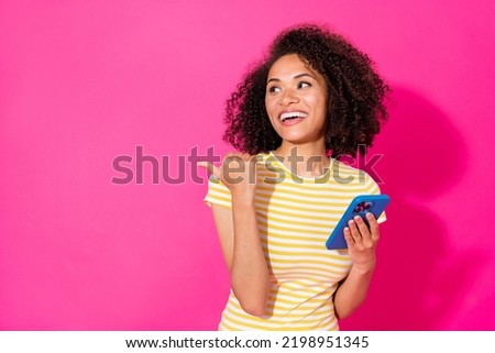 Photo portrait of pretty young girl hold device point copyspace wear trendy yellow striped clothes isolated on bright pink color background