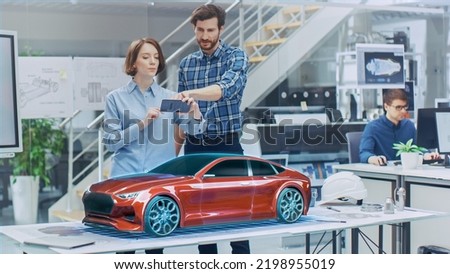 Industrial Design: Automotive Engineer and Designer Working on 3D Electric Car Prototype, Using Smartphone with Augmented Reality. Graphical Engine, Battery, Chassis, Body Collect into Vehicle