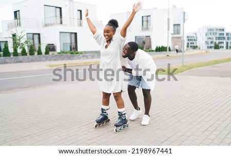 Full length of cheerful African American couple in casual clothes having fun while skating on city street together on blurred background