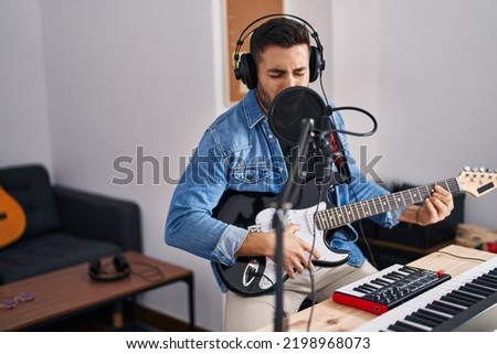 Young hispanic man singing song playing electric guitar at music studio Royalty-Free Stock Photo #2198968073