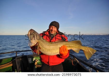 Smiling fisherman holds huge codfish against background of cold North Sea, Barents sea