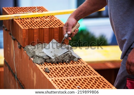 anonymous construction worker on a building site when building a house built a wall of brick. brick wall of a solid house. symbolic image for illegal work and bungling Royalty-Free Stock Photo #219899806