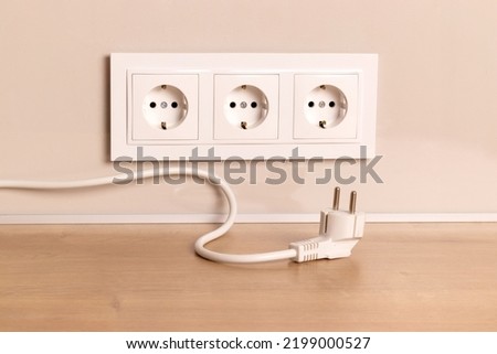 Power cord cable unplugged with group of white european electrical outlets on modern beige wall Royalty-Free Stock Photo #2199000527