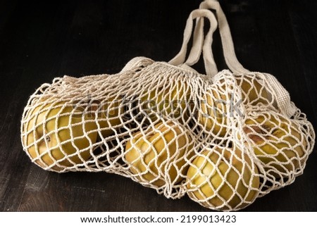 Close-up of white organic net bag with pippin apples, on dark wooden table, black background, horizontal