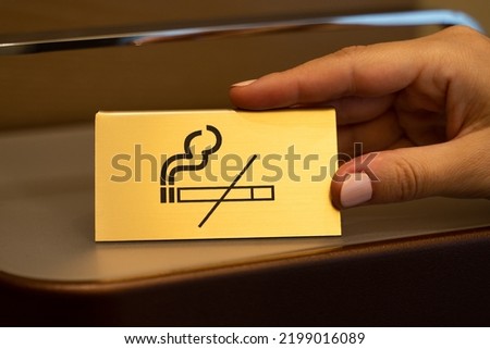 Maid puts golden plate with No Smoking sign picture on wooden shelf in hotel room. Woman takes care of order and comfort of accommodation for guests closeup