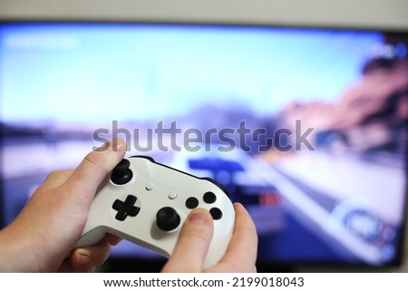 Plays racing games on TV while holding white gamepad