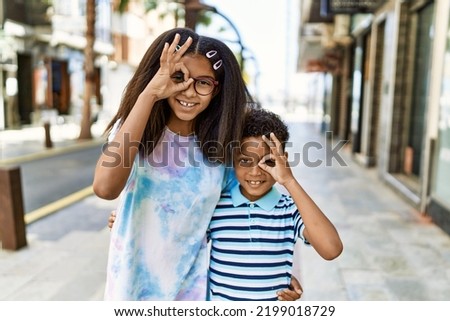 African american family of bother and sister standing at the street smiling happy doing ok sign with hand on eye looking through fingers 
