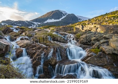 Waterfall with mountains in background with snow on them, evening light with nice colored sky, Gällivare county, Stora sjöfallet nationalpark, Swedish Lapland, Sweden Royalty-Free Stock Photo #2199019169