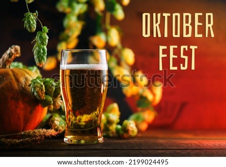 Oktoberfest banner, glass of light beer on a wooden table, branches of green hops, ears of wheat and pumpkin