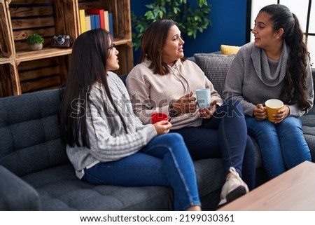 Three woman drinking coffee sitting on sofa at home