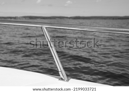 black and white shot of a boat railing (metal rod) and in the background water