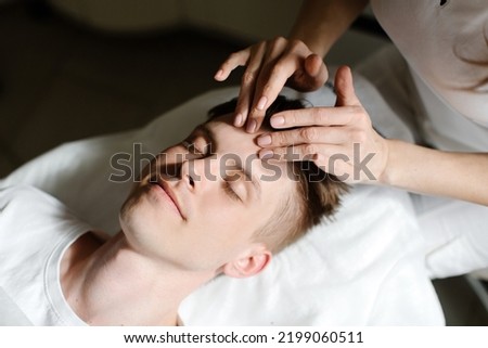 A man lies in a beauty parlor and enjoys a facial massage. Close-up of a man's portrait and woman's hands. High quality photo