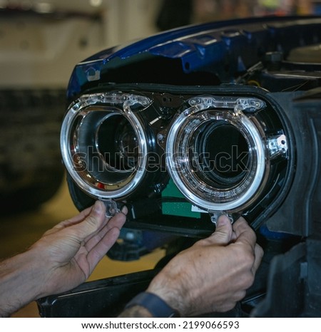 Car headlight in repair close-up. The car mechanic installs the lens in the headlight housing. The concept of a car service.Installation of LED lenses in the headlight. LED lens.Restoration of optics. Royalty-Free Stock Photo #2199066593