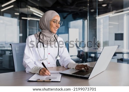 Arab muslim woman in hijab doctor working in modern clinic office with laptop, doctor on paper work in white medical coat with stethoscope and glasses. Royalty-Free Stock Photo #2199073701