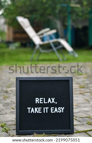 "Relax take it easy" words written on a black letterbox put in the garden with the background of lounge chair in teh garden.