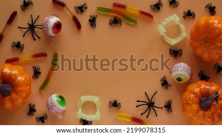Pumpkins,cauldrons,pots,worms,jaws,spiders and candy in the form of eyes on a orange background,top view,copy space.Collection of items for a Halloween party.Holiday card