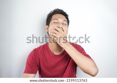 Young asian man wearing t-shirt standing over isolated white background bored yawning tired covering mouth with hand. Restless and sleepiness.