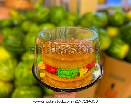 Hand holding a Hamburger cake and blurred watermelons in the background