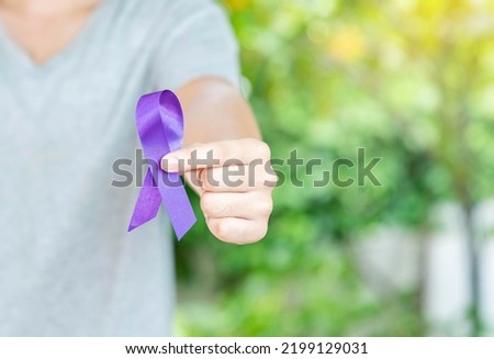 The man in grey shirt show purple in hand on out of focus background. Concept of world cancer day.