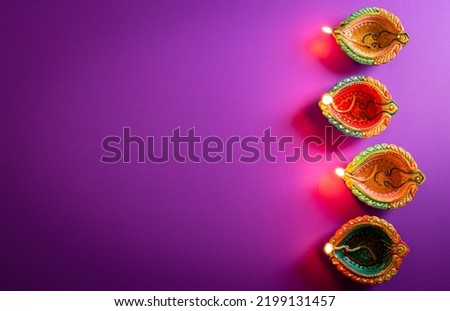 Happy Diwali - Clay Diya lamps lit during Dipavali, Hindu festival of lights celebration. Colorful traditional oil lamp diya on purple background Royalty-Free Stock Photo #2199131457