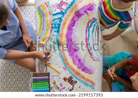 Family mother and kids drawing art picture on paper with multicolored chalks enjoy weekend leisure activity top view. Caring mom spending time with son and daughter happy motherhood relaxing at home