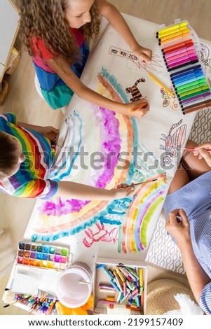 Family mother and kids drawing art picture on paper with multicolored chalks enjoy weekend leisure activity top view. Caring mom spending time with son and daughter happy motherhood relaxing at home
