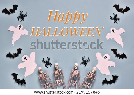 Happy Halloween greeting card. Flat lay composition with text Happy Halloween with the ghosts, spiders, skeletons and bats on light blue background. Postcard for holiday. Top view 