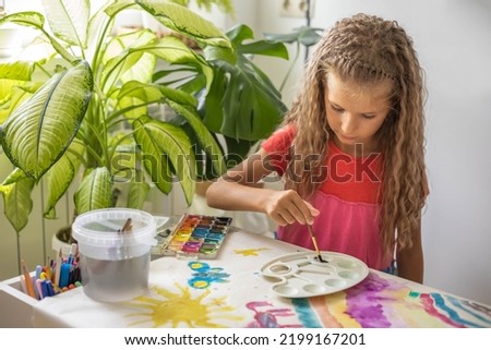 Laughing blonde curly barefoot little girl drawing paper art picture multicolored chalks sitting floor near childish hovel. Relaxed female kid happy childhood preschool early development entertainment Royalty-Free Stock Photo #2199167201