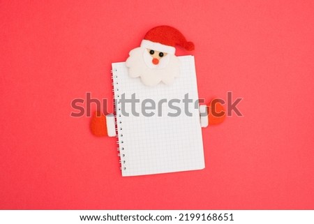 Christmas notebook wire binding blank template design idea. Santa Claus with red cap and winter gloves against pastel pink background.  Copy space for merry christmas message.