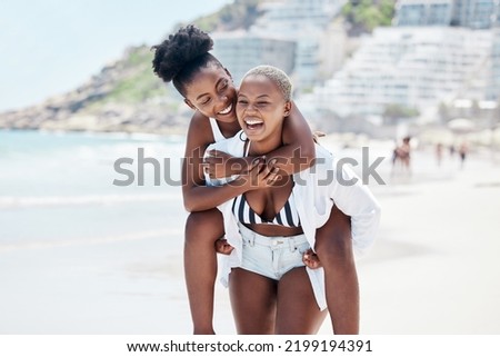 LGBTQ, gay and lesbian black women enjoying a piggyback ride and fun at beach in summer. Friends, dating and trust with female and her girlfriend on holiday, vacation or travel by the coast Royalty-Free Stock Photo #2199194391