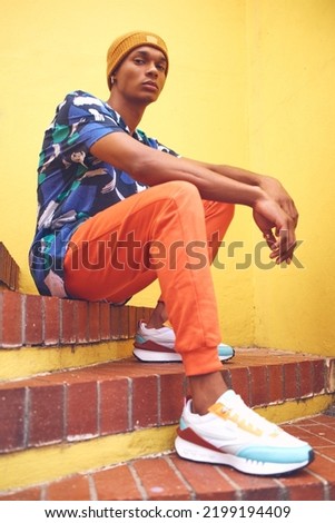 Black man, fashion and street style clothes on cool, trend or attitude model on steps by city wall background on building. Portrait of serious student sitting on stairs in urban punk clothing outdoor