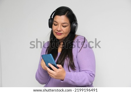 Latino adult woman uses technology with his cell phone and headphones to listen to music, play video games, make video calls, watch series, shopping and date on the app
