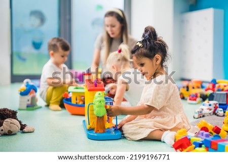 Nursery school. Toddlers and their teacher playing with colorful plastic playhouses, cars and boats. Imagination, creativity, fine motor and gross motor skills development. High quality photo Royalty-Free Stock Photo #2199196771