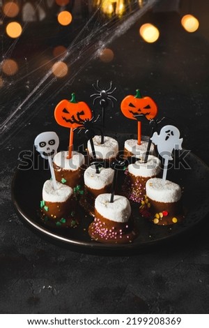  Sweet Halloween treat, marshmallows covered chocolate with sugar and Halloween decorations on a black plate, vertical photo with soft focus, golden bokeh