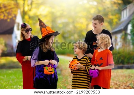 Family trick or treating on Halloween night. Kids in witch and pumpkin costumes trick or treat. Parents and kids have fun with scary dress ups and candy buckets.