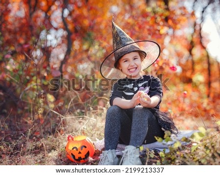 Young girl in black costume goes trick or treating. Little witch, Kids with jack-o-lantern. Children with candy bucket in fall forest. Happy Halloween.