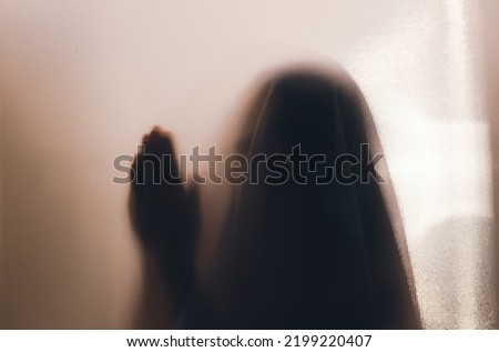 Horror ghost woman praying behind the matte glass. Halloween festival concept.