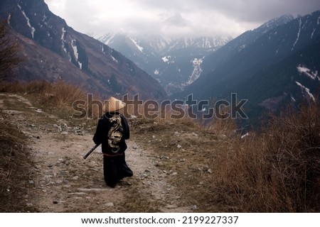 Rear view of a Young boy dressed as Samurai with the painted dragon on Kimono walking by the mountain trail in the cloudy weather Royalty-Free Stock Photo #2199227337
