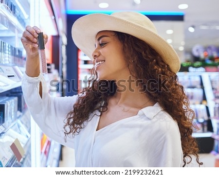 Beauty, cosmetic and makeup customer in a store with product choice from retail shelf and happiness. Young, happy black woman shopping cosmetics in a shop and reading lipstick label for review Royalty-Free Stock Photo #2199232621