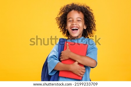 Delighted African American boy in glasses laughing for camera and reading book  while having fun during school students against yellow background Royalty-Free Stock Photo #2199233709