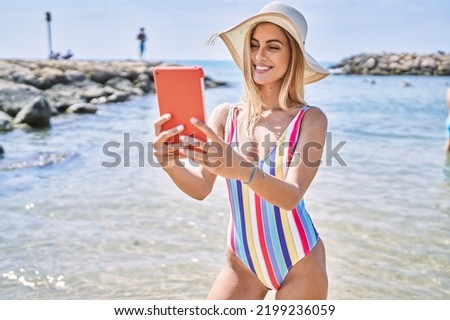 Young blonde girl wearing summer hat make selfie by the touchpad at the beach.