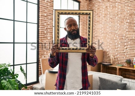 African american man putting face in empty frame smiling looking to the side and staring away thinking. 