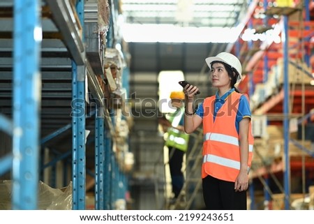 Female warehouse worker checking inventory boxes with barcode scanner on shelf in a large warehouse