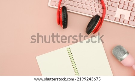 Red wireless headphones, microphone and notepad on pink background. Technology and audio equipment concept