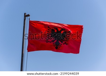 Albania flag. Albanian flag on a flagpole waving on a bright blue sky background.