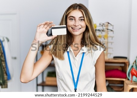 Young blonde woman working as manager at retail boutique holding credit card looking positive and happy standing and smiling with a confident smile showing teeth 