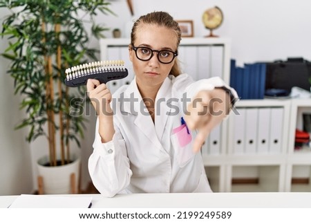 Young caucasian woman holding teeth whitening palette looking unhappy and angry showing rejection and negative with thumbs down gesture. bad expression. 