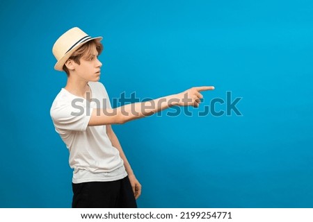 Young teen man points palms aside isolated on blue. Friendly well-looking boy paying your attention at copy space, best deal, sale, presenting novelty