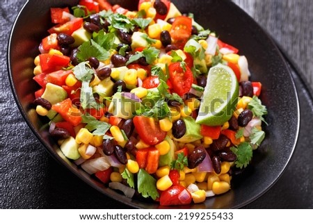 cowboy bean salad, texas caviar with black bean, tomatoes, avocado, red bell pepper, corn, coriander  in black bowl , close-up