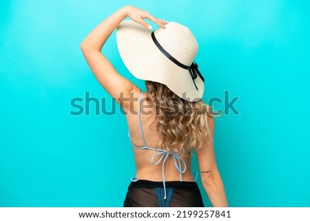 Young caucasian woman isolated on blue background in swimsuit and in back position
